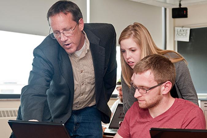 Professor with students looking at laptop